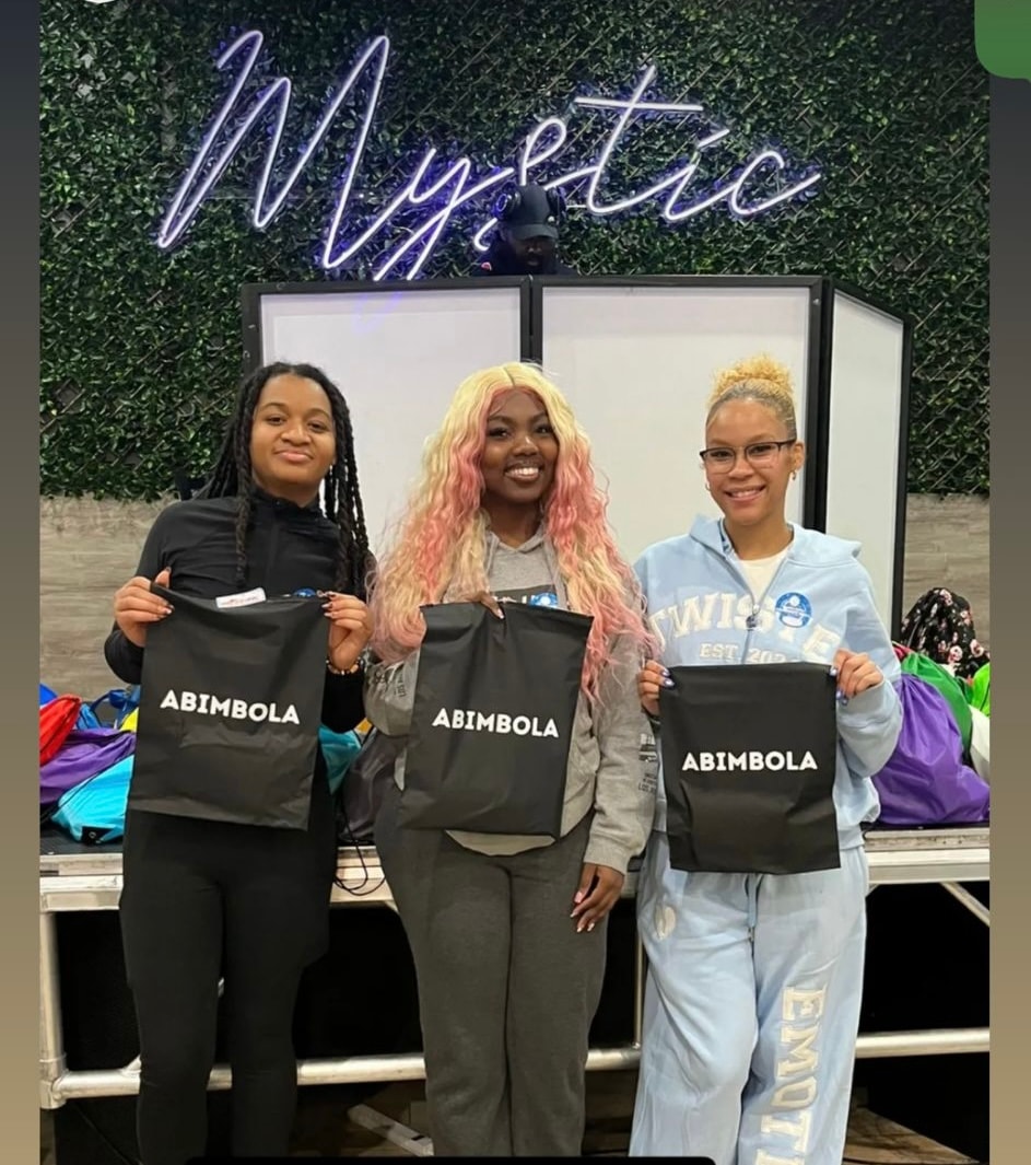 ABIMBOLA community donation event — three women holding ABIMBOLA bags